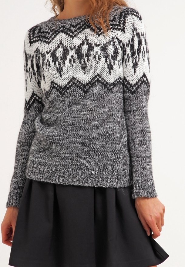 Donna che indossa un maglione grigio lavorato a maglia con motivi geometrici in bianco e nero, abbinato a una gonna plissettata nera.