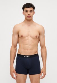Marineblaue Boxer-Shorts aus einem weichen, dehnbaren Material mit einem schwarzen Bund, der das "BOSS"-Logo in Weiß trägt. Enganliegendes Design.