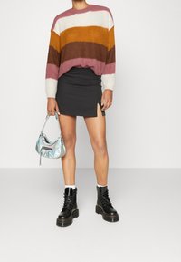 Maglione lavorato a maglia con strisce rosa, bianche, senape e marroni; mini gonna nera con spacco laterale; borsa iridescente; stivali neri con lacci.