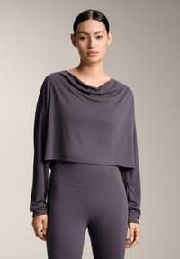 Sivi krojeni dugih rukava top s visokim ovratnikom i prilagođenim siluetom, napravljen od mekog, rastezljivog materijala. Uparen s odgovarajućim krojenim hlačama.