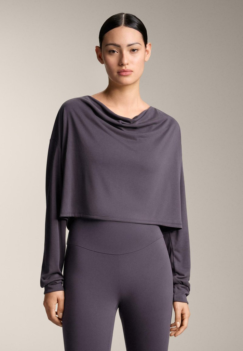 Sivi krojeni dugih rukava top s visokim ovratnikom i prilagođenim siluetom, napravljen od mekog, rastezljivog materijala. Uparen s odgovarajućim krojenim hlačama.