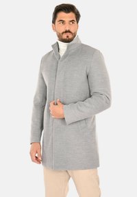 Cappotto in lana grigio chiaro con colletto alto, silhouette dritta e maniche lunghe. Texture liscia, design minimalista e tasche laterali.