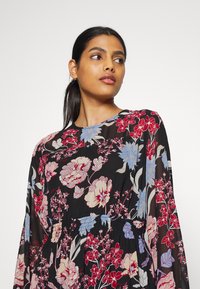 Vestido maxi floral com um tecido preto transparente adornado com flores vermelhas, rosas e azuis. Leve, com mangas longas e uma cintura franzida.