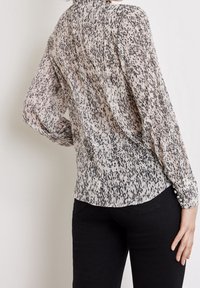 Blouse à manches longues en tissu transparent avec un motif abstrait noir et crème, dotée d'un col montant et de boutons sur les poignets.