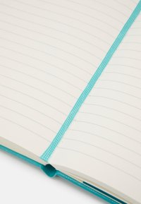 Quaderno turchese con pagine a righe, dotato di copertina morbida e dorso testurizzato. La rilegatura è fissata con un filo turchese coordinato.