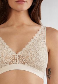 Krajkový bralette v nude barvě, s vroubkovaným okrajem, květinovým vzorem a měkkou, elastickou tkaninou s hladkým páskem dole.