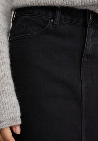 Črne denim hlače s visokim pasom, z gumbom za zapiranje in stranskimi žepi. Tkanina ima mehak občutek s subtilnimi odstopanji v tonu.