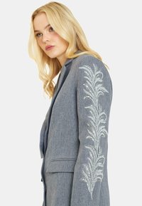 Blazer grigio con finitura testurizzata, caratterizzato da ricami floreali in paillettes blu sulla manica sinistra e un design colletto a scollo.