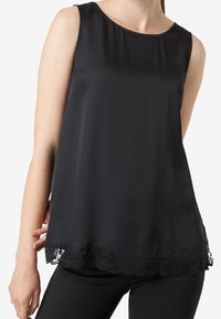 Svart ärmlös topp i mjukt material, med en scalloped spetskant nederst. Minimalistisk design med rund halsringning.