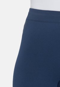 Leggings azzurri a vita alta realizzati in tessuto elasticizzato con una consistenza liscia e un elastico a costine in vita. Nessuna hardware o motivi visibili.