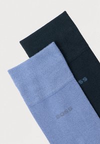 To par sokker: ett i lyseblått og ett i mørkeblått, med en strukturert overflate og en subtil logo på mansjettene.