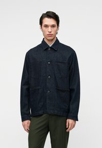 Chaqueta de mezclilla oscura con cuello tipo solapa, cierre frontal de botones y dos bolsillos en el pecho. Presenta un corte relajado y una tela texturizada.