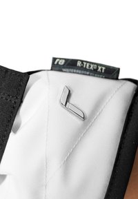 Tissu noir avec une surface texturée et une doublure blanche, présentant un épinglette logo en métal argenté dans un design élégant et angulaire.