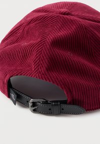 Boné de cordura em cor mármore com sulcos texturizados, apresentando uma faixa de couro preto ajustável com ferragens metálicas na parte de trás.