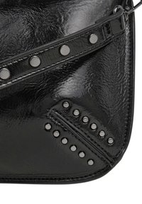 Borsa in vernice nera con borchie argento, caratterizzata da un dettaglio di cucitura diagonale. La superficie è liscia con una finitura lucida e dettagli testurizzati.