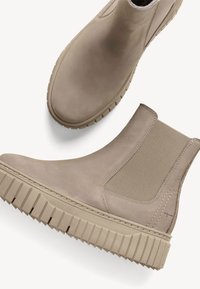 Beige Chelsea boots with elastic side panels and chunky rubber soles. Smooth leather upper with subtle stitching detail.