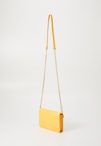 Gul crossbody veske laget av glatt materiale med klaffelukking, har en avtakbar gullkjede stropp og en dekorativ logo plate.