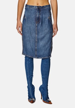 Person trägt einen midilangen Jeansrock über passenden Jeansstiefeln mit hohen Absätzen, spitzen braunen Zehen und silbernen Verzierungen.