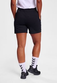Sorte treningshorts med elastisk midjebånd, sammen med sorte joggesko og hvite sokker med et chevronmønster.