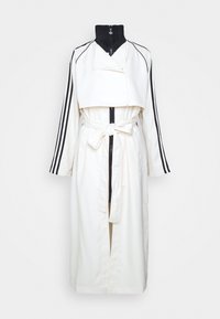 Krämfärgad trenchcoat med svart hög krage, kort design, långa ärmar med tre svarta ränder och ett knytbälte i midjan.