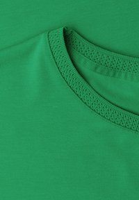 Gros plan d'un t-shirt vert à col rond montrant un tissu lisse et une couture de col côtelée texturée.