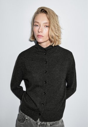 Cardigan en maille gris foncé avec un col mandarin, doté de boutons sombres et d'une coupe décontractée, fabriqué dans un tissu doux et texturé.