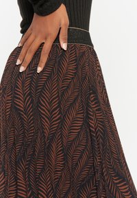 Svart kjol med bladmönster i rosttoner, med ribbad midja som har en metallisk gyllen linje. Slät, flödande tygtextur.