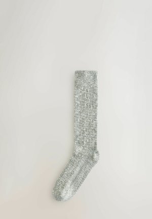 Enkele grijze gebreide sok met een geribde boord, plat gelegd op een lichte neutrale achtergrond.