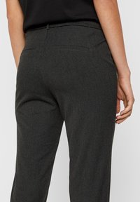 Dark grey, tailored trousers made of textured fabric with a drawstring waistband and two back pockets, shown from the back.