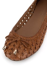 Brown woven leather ballet flat with rounded toe, decorative bow with gold metal tips, and smooth inner sole.