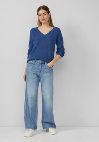 Niebieski sweter w splot w prążki z dekoltem w kształcie litery V, zestawiony z jasnoniebieskimi spodniami typu wide-leg i białymi sneakersami. Posiada długie rękawy i luźny krój.