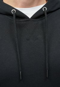 Fekete kapucnis pulóver elülső kenguruzsebbel, fémből készült fülön átvezetett húzózsinórokkal és texturált varrással a nyakkivágásnál.