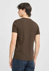 T-shirt marron à manches courtes avec un col ras du cou et une texture lisse, associé à un jean en denim foncé ; la vue de dos montre les détails de coupe et de design.