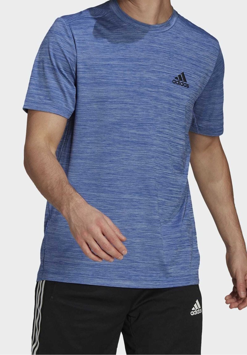 Sininen urheilupaita, jossa on tekstuurikuosi, pyöreä pääntie, lyhyet hihat ja musta adidas-logo vasemmassa rinnassa. Yhdistetty mustiin shortseihin.