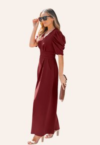 Vestido maxi burdeos con mangas abullonadas, cintura ceñida y falda plisada. Llevado con sandalias de tacón bloque transparente y un clutch marrón.