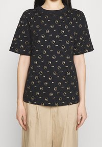 Czarna koszulka z krótkim rękawem z powtarzającym się wzorem złotych okręgów i logo Nike. Wykonana z miękkiej bawełny o luźnym kroju.