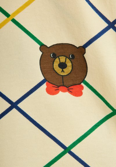 Tela crema con un gráfico de oso pardo que presenta un hocico dorado y una pajarita roja. Líneas diagonales coloridas en verde, azul y amarillo se superponen.