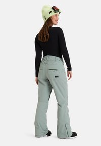 Muntgroene sneeuwbroeken met een relaxed fit, voorzien van ritszakken en een verstelbare taille, gecombineerd met een zwart langemouwen shirt en een lichtgroene beanie.