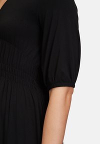 Schwarzes Kleid mit kurzen, gepufften Ärmeln, ausgestattet mit einem elastischen Bund und weichem, strukturiertem Stoff. Das Design umfasst Raffungen am Oberteil.