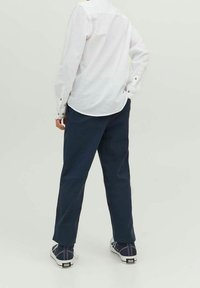 Biała koszula z długim rękawem z detalami guzików, zestawiona z granatowymi spodniami bawełnianymi i granatowymi trampkami z białymi podeszwami oraz akcentami tekstylnymi.