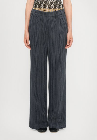 Pantaloni evazați de culoare bleumarin închis, cu un model texturat de herringbone. Talie elastică și material neted, asortați cu încălțăminte neagră.