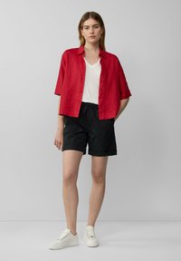 Camisa de lino roja de manga corta, camiseta blanca de cuello en V debajo, pantalones cortos negros remangados y zapatillas blancas. Diseño sencillo y ajuste relajado.