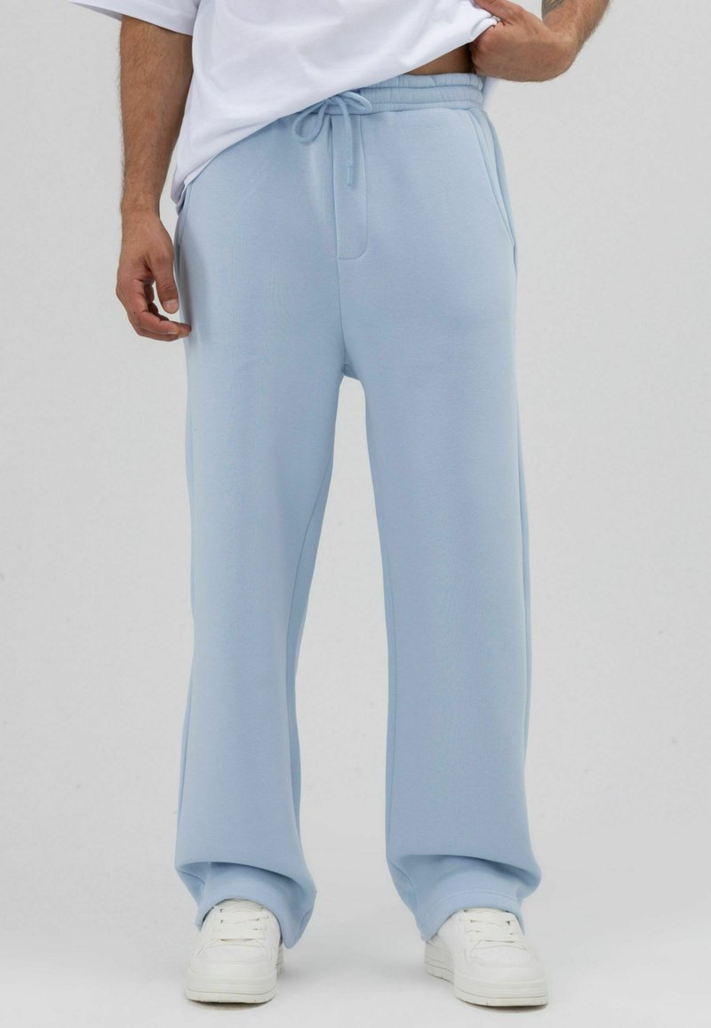 Pantalon de survêtement bleu clair en tissu doux ; coupe ample avec taille élastique et poches latérales ; porté avec des baskets blanches.