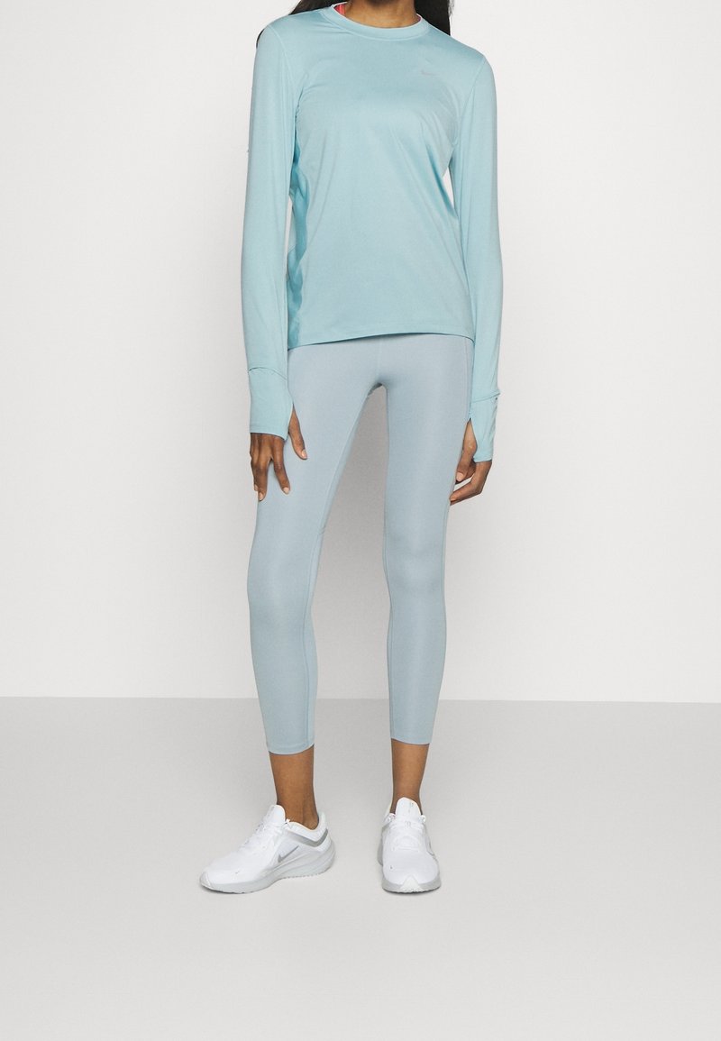 Hellblaues Langarmoberteil mit Rundhalsausschnitt, kombiniert mit passenden Leggings. Weiße Sportschuhe runden das Outfit ab. Glatte Textur, figurbetontes Design.
