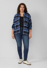 Karierte Hemd in Blau und Schwarz, langärmlig, kombiniert mit dunklen Skinny Jeans und lässigen, hellen Sneakern. Glattes Material, Knopfverschluss.