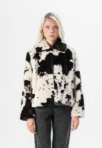 Faux-Fur-Jacke mit einem schwarz-weißen Kuhflecken-Design, einem Kragen und weiten Ärmeln. Strukturierter, weicher Stoff mit einer kastigen Form.