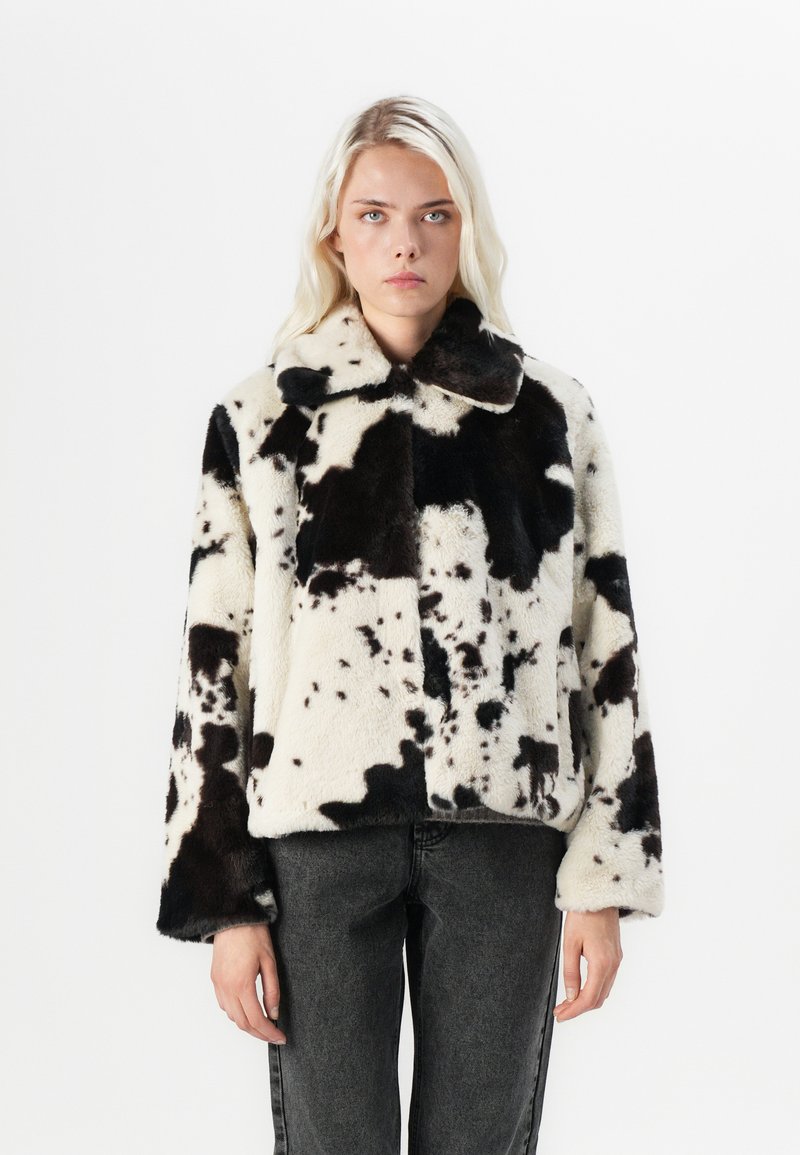 Faux-Fur-Jacke mit einem schwarz-weißen Kuhflecken-Design, einem Kragen und weiten Ärmeln. Strukturierter, weicher Stoff mit einer kastigen Form.