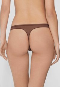 Brauner Stringtanga mit minimaler Bedeckung, mit weicher Textur und elastischem Bund, von hinten gezeigt vor einem glatten Hautfarbigen Hintergrund.
