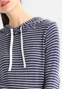 En marinblå och vitrandig hoodie i mjukt tyg, med dragsko, avslappnad passform och en avslappnad halslinjedesign.