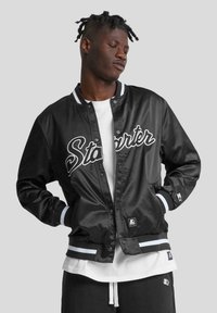 Veste bomber en satin noir avec logo "Starter" brodé en blanc, poignets et ceinture rayés contrastants, fermeture à boutons-pression et patch logo.